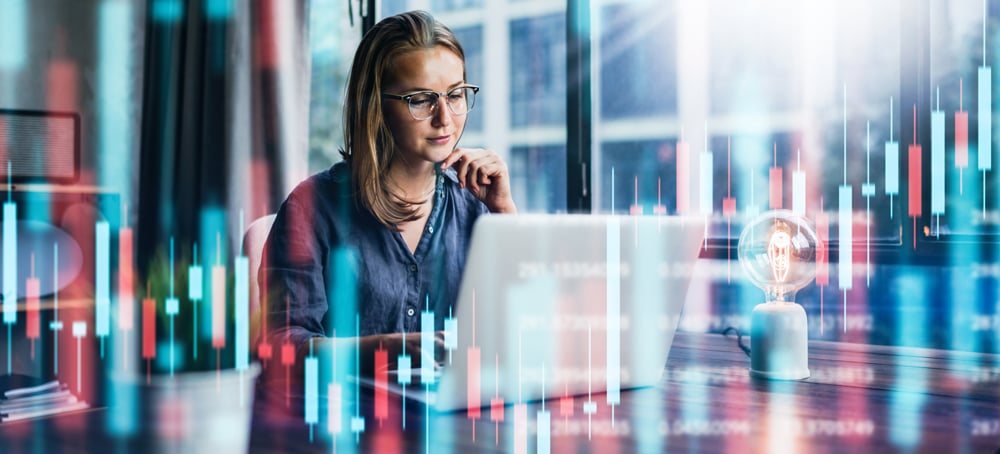 Woman sitting at desk in front of computer with candlestick graph image overlay